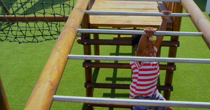 High angle view of African American schoolboy playing on horizontal ladder in school playground