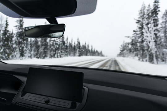 View from inside a modern car driving on a snowy road through a winter pine forest, POV dashboard perspective of an automotive winter road trip in Lapland