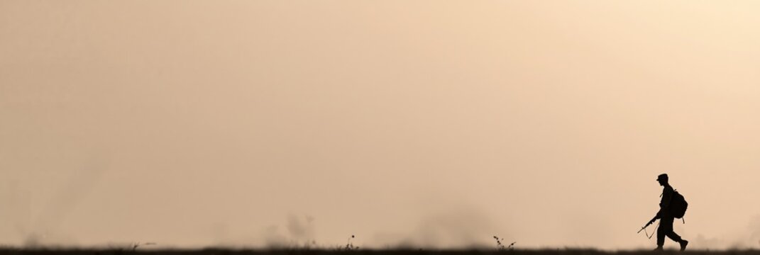 Silhouette of soldier walking across open landscape at sunrise, beige and tan color tones representing memorial reflection