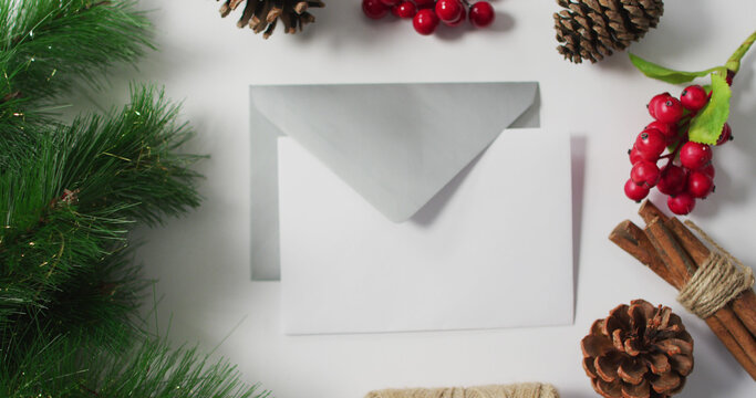Image of christmas pine cones, tree and red berry decorations with envelopes on white background