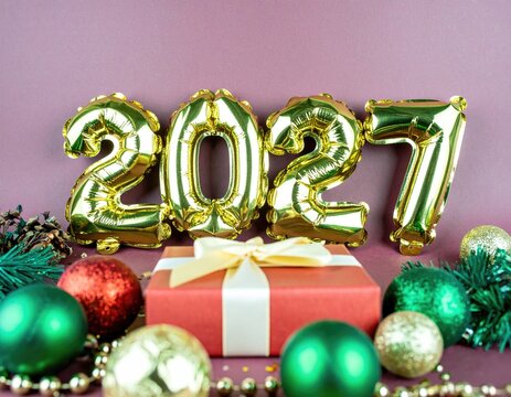 Golden balloons spell out 2027 on a red background surrounded by festive decorations, christmas ornaments, and a gift box