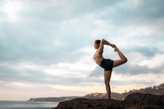 Asian woman enjoying the health benefits of outdoor yoga on an ocean rock cliff