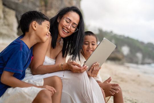 Asian mother and children using a digital tablet for online learning on the beach