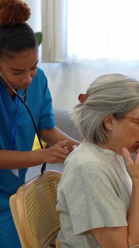 Young hispanic nurse listening to the back of an elderly female patient with stethoscope during a home visit