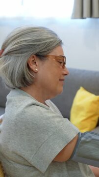 Elderly woman with gray hair resting calmly on chair while undergoing a blood pressure check at home