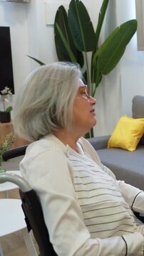 Caring latina home health nurse feeding soup and giving water to an elderly woman sitting in a wheelchair indoors