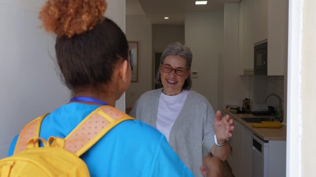 Elderly woman opening apartment door and hugging visiting latina home health nurse, greeting each other with warm smiles
