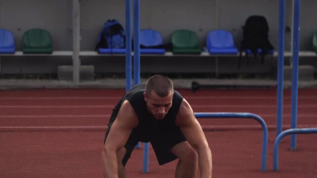 Muscular athlete performing burpee jump exercise for cardio and strength training at outdoor stadium track
