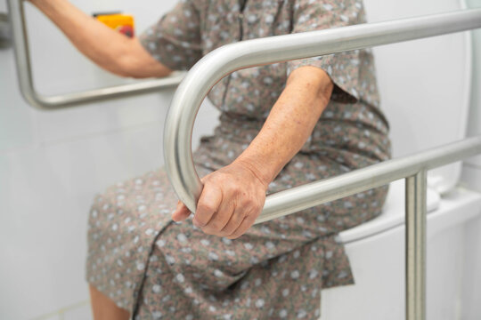 Asian elderly woman use toilet security support rail in bathroom.