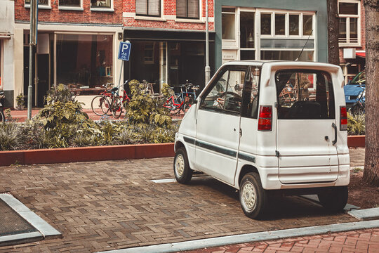 Amsterdam, Netherlands. Retro white microcar parked on a vintage brick street. Surrounded by classic brick architecture, traditional bicycles, and historic city charm.