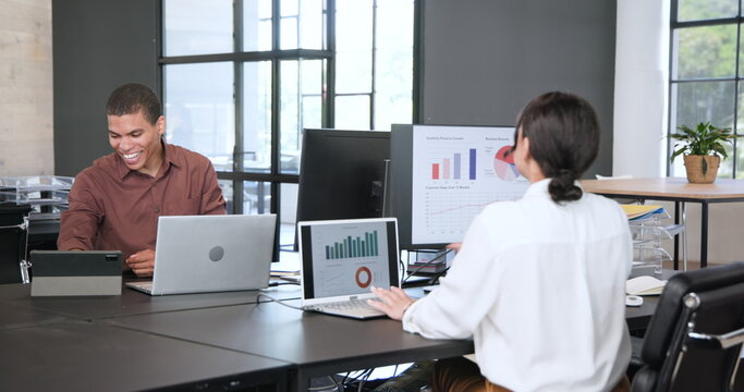 Multiracial businesswoman and multiracial businessman talking and using laptop computers in modern o