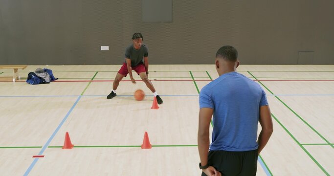 Receiving basketball, African American youth dribbling through orange cones in gym during drill