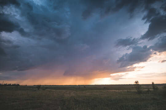 A cloudy evening sky at sunset over the Kazakh steppes, featuring rain clouds and sunbeams&mdash;a summer landscape under overcast skies, with rain visible on the horizon