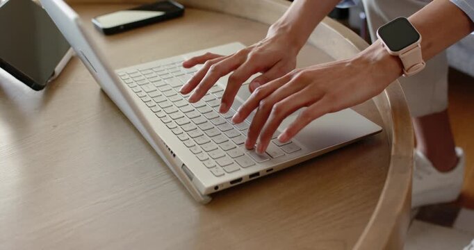 Hands typing and repositioning on white laptop at round wooden table with smartphone nearby