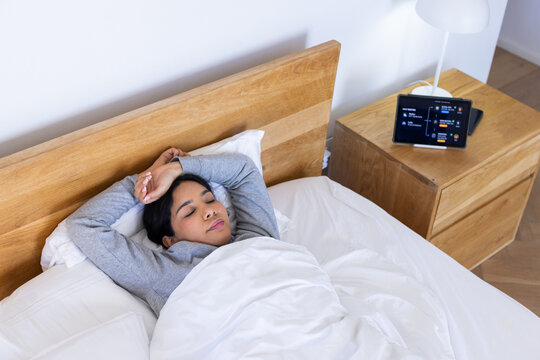 Asian woman lying in bed resting with closed eyes and hands behind head under white duvet