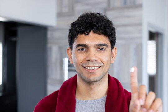 African American man raising index finger while wearing maroon robe and gray shirt in kitchen