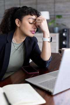 African American woman sitting at wooden desk and pressing fingers to forehead near laptop
