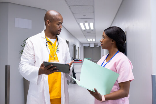 African American professionals in scrubs talking in hospital corridor holding tablet and folder