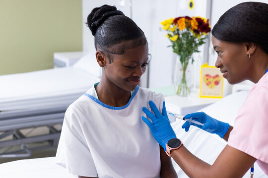 African American female healthcare worker giving injection to girl sitting in exam room