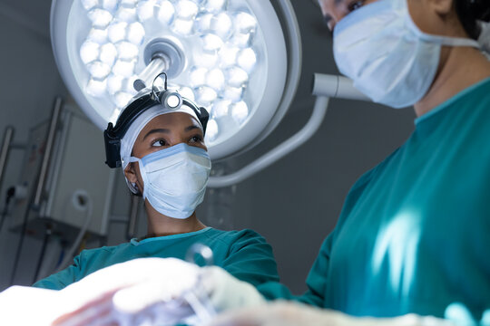 Indian female surgeon wearing headlamp and teal scrubs looking upward under surgical light