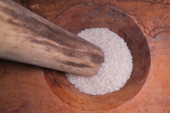 Traditional wooden mortar and pestle pounding white rice grains