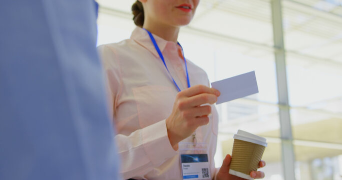 A young Caucasian businesswoman presents her business card to a colleague at a seminar.