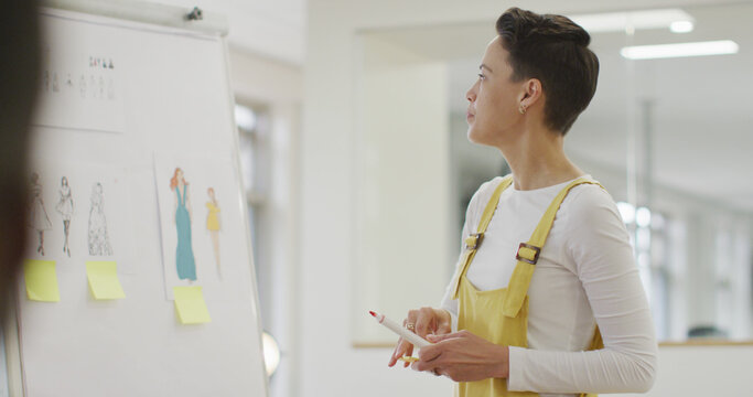 Caucasian businesswoman standing at whiteboard, talking, giving presentation in office