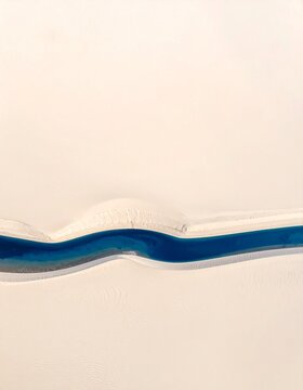 Deep blue liquid flowing in a curved stream across a pale cream surface, minimal abstract with copy space