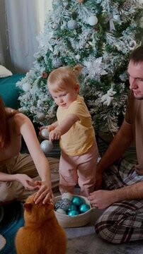 A Family Celebrating Together as a Child Joyfully Engages with Decorated Holiday Ornaments Amidst a Festive Atmosphere by a Christmas Tree