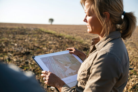 A farm worker closely examining a detailed map in an open field, highlighting the essential role of planning in contemporary agriculture for effective land use.