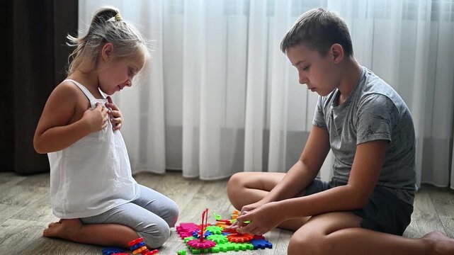 Boy and girl playing with bright gear construction toy on wooden floor near window. Children enjoy developmental activity together, demonstrating teamwork and learning at home.