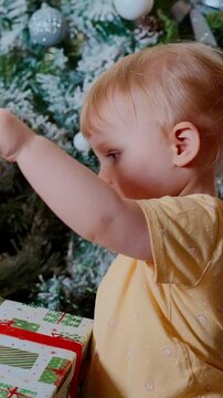 A Curious Toddler Interacts with a Festive Christmas Present Beneath a Beautifully Decorated Tree, Capturing the Spirit of Holiday Joy and Innocence