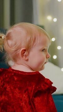 Adorable Toddler in Sparkling Red Outfit Sitting on a Couch with Warm Ambient Lighting and a Soft Toy in a Cozy Room Setting