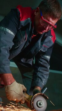 A focused worker uses an angle grinder to cut metal in a dimly-lit workshop, showcasing expertise and precision in metalworking tasks and craftsmanship.