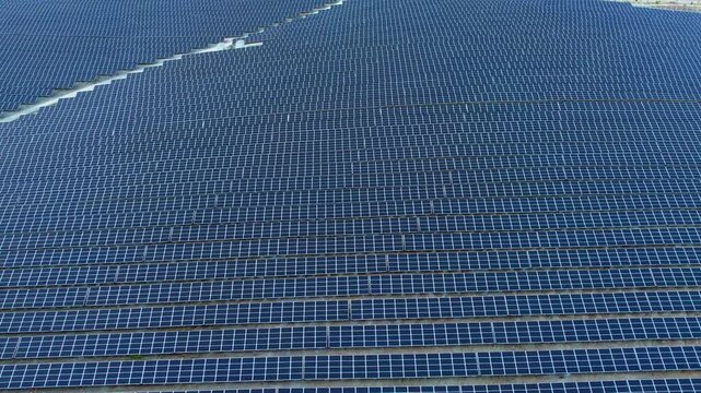 Aerial view of an enormous solar farm featuring endless rows of blue photovoltaic panels arranged in precise geometric patterns, showcasing renewable energy infrastructure and clean power generation.