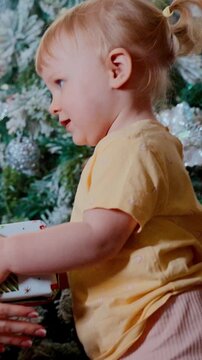A Small Child in a Yellow Shirt Enjoys the Festive Atmosphere Near a Christmas Tree Surrounded by Decorations and Gifts During a Joyful Celebration