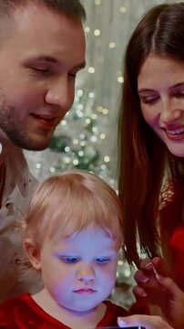 A Young Family Enjoying Quality Time Together While Engaged with a Smartphone Surrounded by Festive Holiday Decorations and Warm Holiday Atmosphere