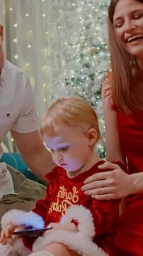A Joyful Family Moment as Parents Admire Their Child Engaged with a Phone During a Cozy Holiday Gathering Surrounded by Festive Decorations and Lights
