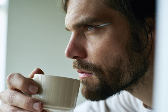 A close-up of a thoughtful man with a beard enjoying a cup of coffee, capturing depth in his expressions and showcasing a moment of reflection and introspection.