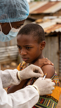 Doctor injecting vaccine into arm of african adolescent boy. Medical worker wearing clinical protective clothing providing immunization in poverty area during global pandemic virus outbreak.