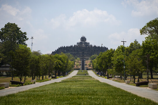 MAGELANG, INDONESIA - OCTOBER 21, 2026: A long grass-lined path leads visitors toward Borobudur Temple, the ninth-century Buddhist monument, with scaffolding on its top stupa during restoration.