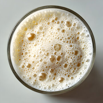 Glass of creamy milk with frothy top on white background. High angle view of refreshing dairy beverage. Minimalist, clean studio shot of healthy drink. Great for breakfast, smoothies, or recipes.