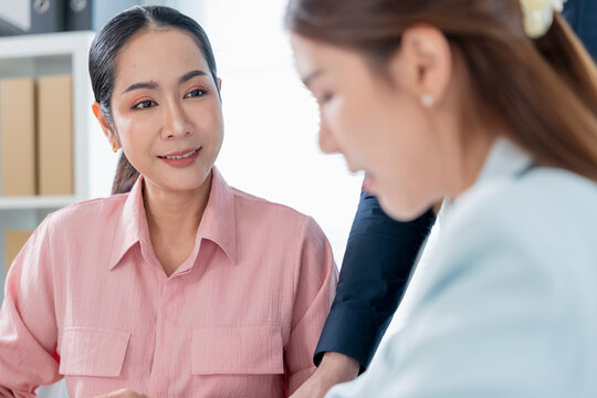 Smiling mature Asian businesswoman mentor listening attentively to younger female colleague and giving supportive advice during conversation in bright office