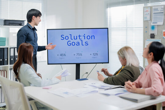 Young Asian businessman presenting data visualization of market size, market trends and competitor market share on screen to colleagues in meeting room