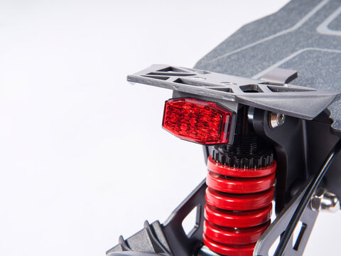 Close-up of electric scooter rear LED tail light and red coil suspension shock absorber, isolated white background