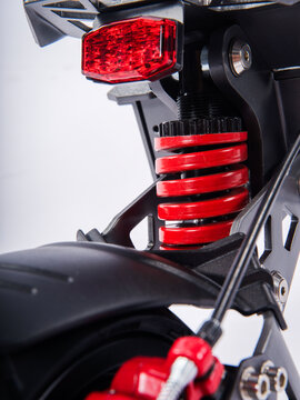 Close-up of electric scooter rear LED tail light and red coil suspension shock absorber, isolated white background