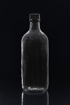 Empty glass bottle with water drops on black background