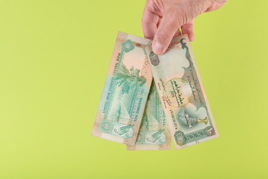 Hand holding dirhams banknotes of United Arab Emirates on green background