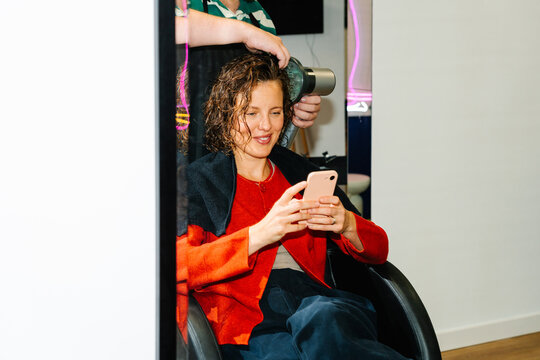 Woman using smartphone while hair is styled