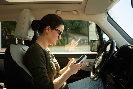 Woman sitting in car checking phone on a sunny day
